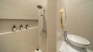 Moderni kylpyhuone, jossa on suihku, pesuallas ja hyllyllä kolme pulloa shampoota.