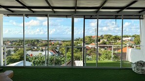 A room with a large window offering a view of a residential area with houses and greenery. - Chic 3BR in Nusa Dua w Ocean View+Cinema+Rooftop (Kabupaten Badung)