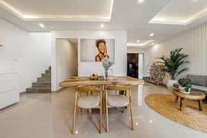 A modern interior with a dining area featuring a wooden table and chairs, a staircase, and a living area with a sofa and a coffee table. - Chic 3BR in Nusa Dua w Ocean View+Cinema+Rooftop (Kabupaten Badung)