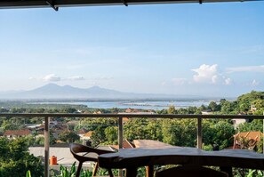 Un balcone con vista su un paesaggio costiero, che include un corpo d'acqua e montagne in lontananza.
