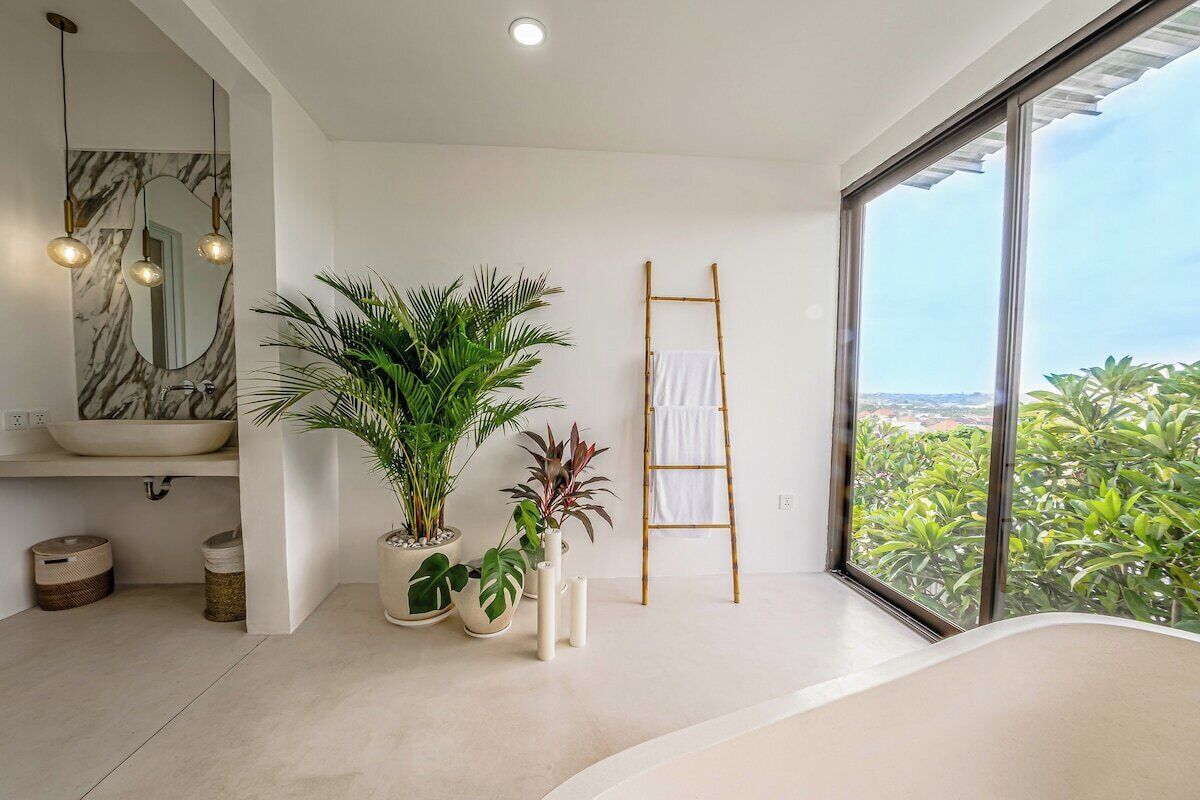 Un baño moderno con un amplio ventanal, un lavabo de mármol y varias plantas en macetas.