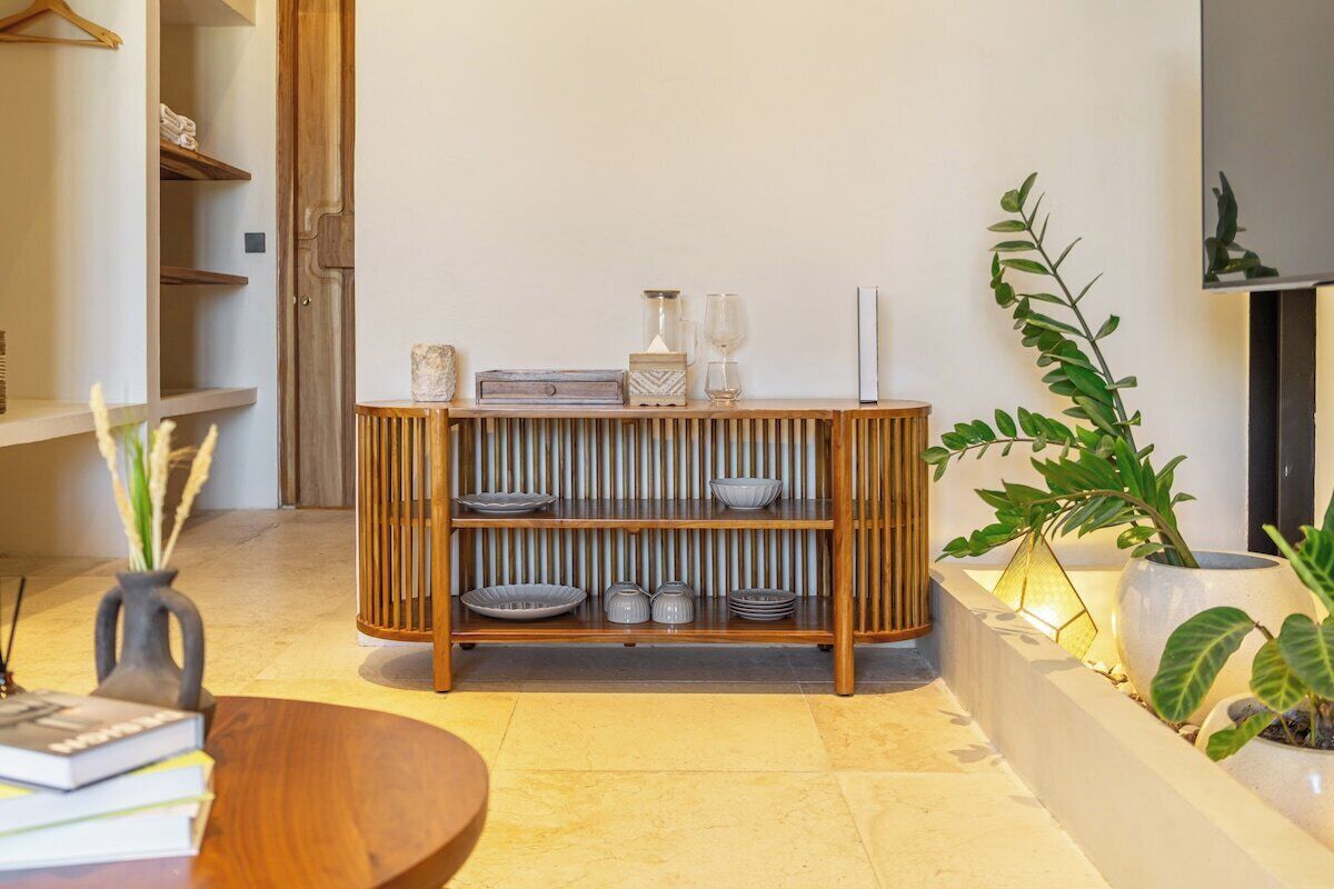Een modern interieur met een houten console waarop decoratieve objecten staan, een ronde tafel met boeken en een plant in een pot.