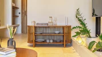 Een modern interieur met een houten console waarop decoratieve objecten staan, een ronde tafel met boeken en een plant in een pot.