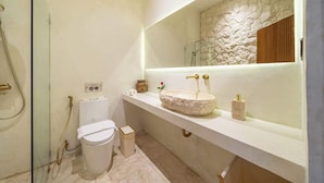 Et stilfuldt badeværelse med vask i sten, toilet og bruseniche.