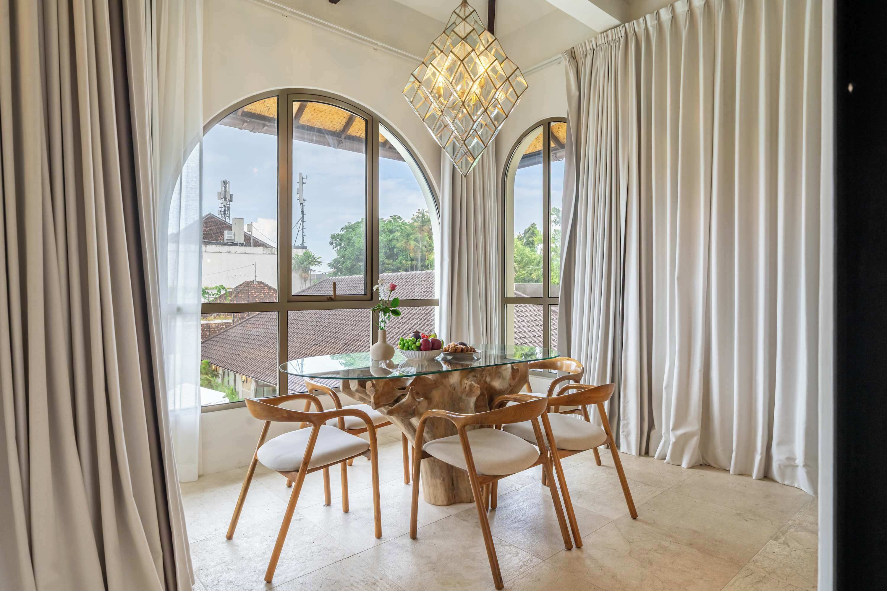 A dining area with a glass-top table, six wooden chairs, and a chandelier.