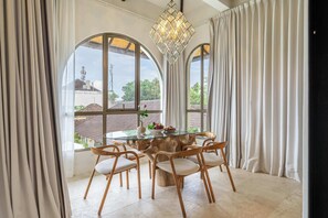A dining area with a glass-top table, six wooden chairs, and a chandelier. - Cozy 2-Storey Flat by Sanur Beach w Pool & Office (Kota Denpasar)