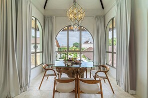 Un comedor con mesa de vidrio, sillas de madera y una araña.