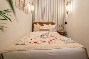 A neatly made bed with a beige blanket and pillows, a bedside lamp, and a wall-mounted light fixture. - Cozy 2-Storey Flat by Sanur Beach w Pool & Office (Kota Denpasar)