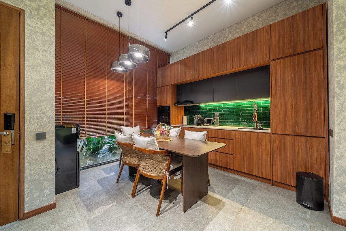 Une cuisine moderne avec des meubles en bois, une table à manger avec des chaises et un revêtement mural vert.