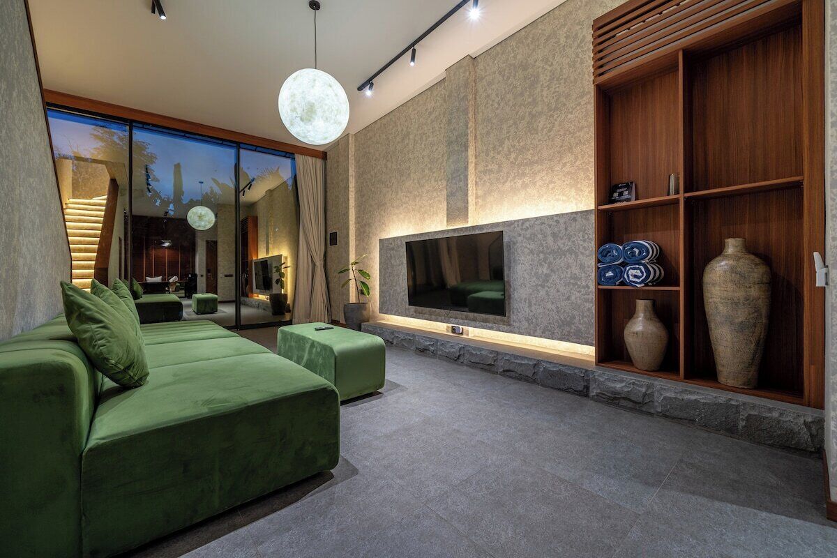 Un salon moderne avec un canapé vert, un téléviseur à écran plat et un mur décoratif en pierre.