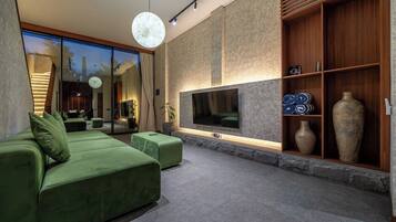 Un salon moderne avec un canapé vert, un téléviseur à écran plat et un mur décoratif en pierre.