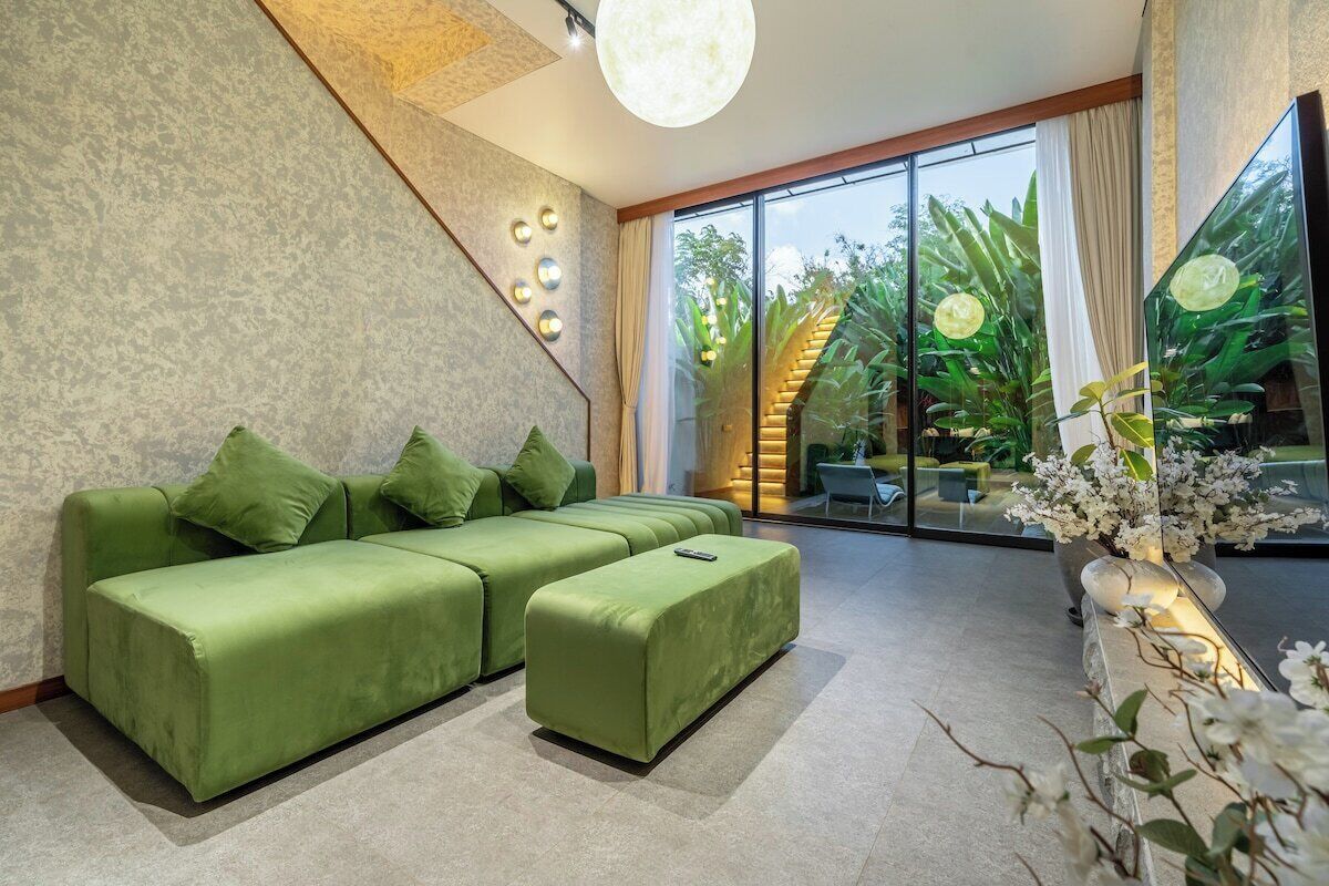 Un salon moderne avec un canapé d’angle, un petit pouf et une grande fenêtre donnant sur un paysage verdoyant.