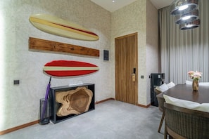 A modern interior with a dining area, a wooden door, and surfboards displayed on the wall. - U Vulla 12 - Modern 2BR Villa w Beach Nearby & Private Pool (Badung Regency)