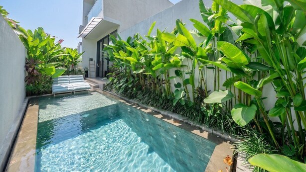Una piscina de diseño moderno, rodeada de abundante vegetación y un estilo arquitectónico minimalista.