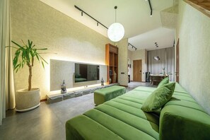 A modern living room with a green sofa, a large flat-screen TV, and a potted plant. - U Vulla 12 - Modern 2BR Villa w Beach Nearby & Private Pool (Badung Regency)