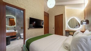 Habitación de hotel con cama, televisión, espejo y baño con lavabo e inodoro.