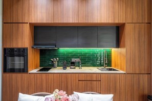 A modern kitchen with wooden cabinets, a built-in oven, a coffee machine, and a green backsplash. - U Vulla 12 - Modern 2BR Villa w Beach Nearby & Private Pool (Badung Regency)
