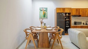 A dining area with a wooden table and chairs, a kitchen with wooden cabinets, and a sofa. - Designer 3BR Villa by Sanur Beach • Pool & Rooftop (Denpasar Selatan)