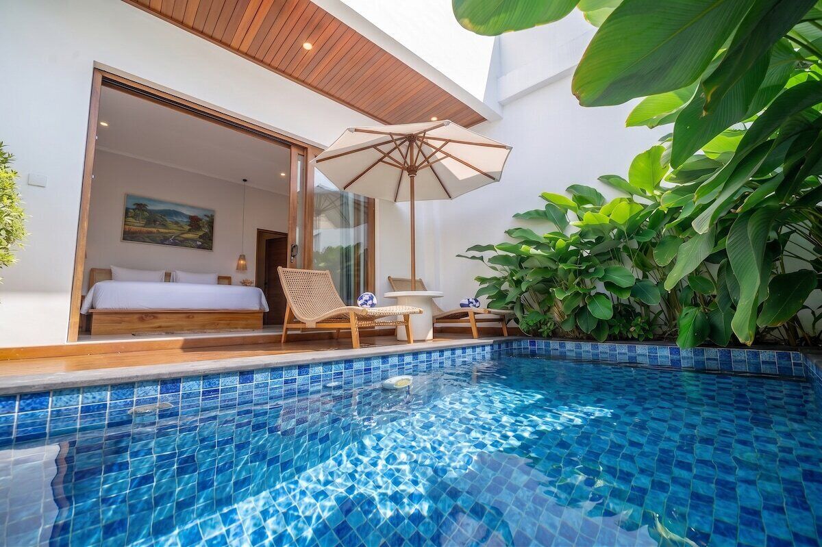 A modern outdoor pool area with a glass-enclosed bedroom, lounge chairs, and a large umbrella.