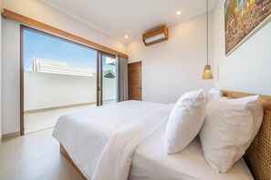 A bedroom with a bed, a sliding glass door leading to a balcony, and a painting on the wall. - Designer 3BR Villa by Sanur Beach • Pool & Rooftop (Denpasar Selatan)