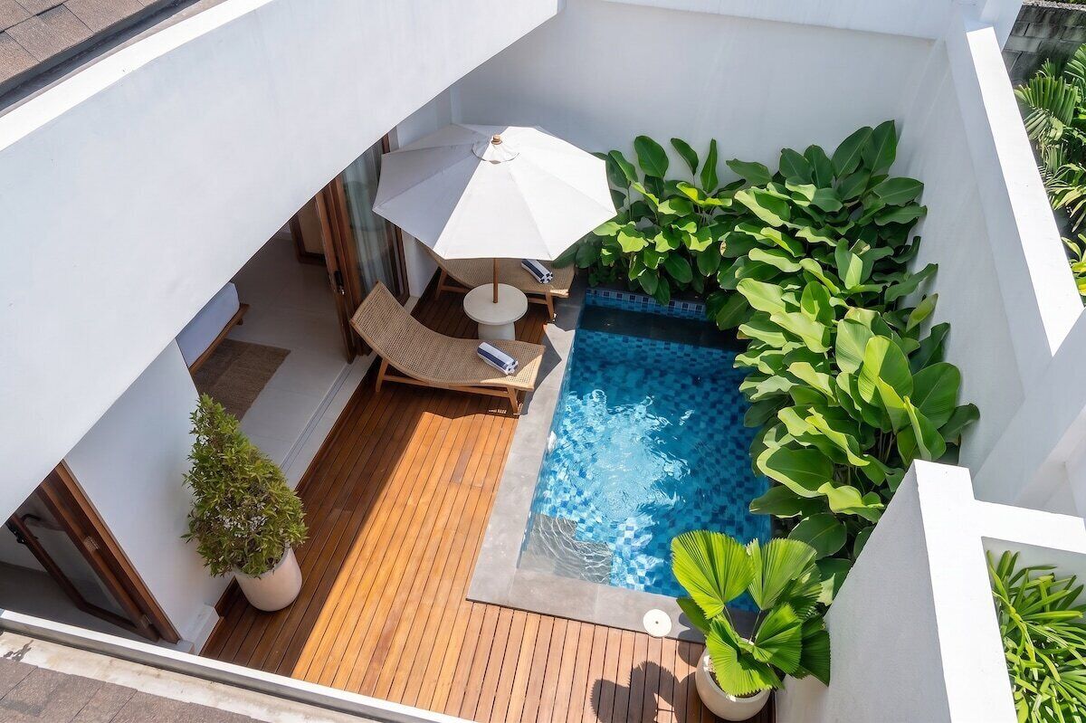 A rooftop pool area with a wooden deck, a lounge chair, a small table, and a white umbrella.