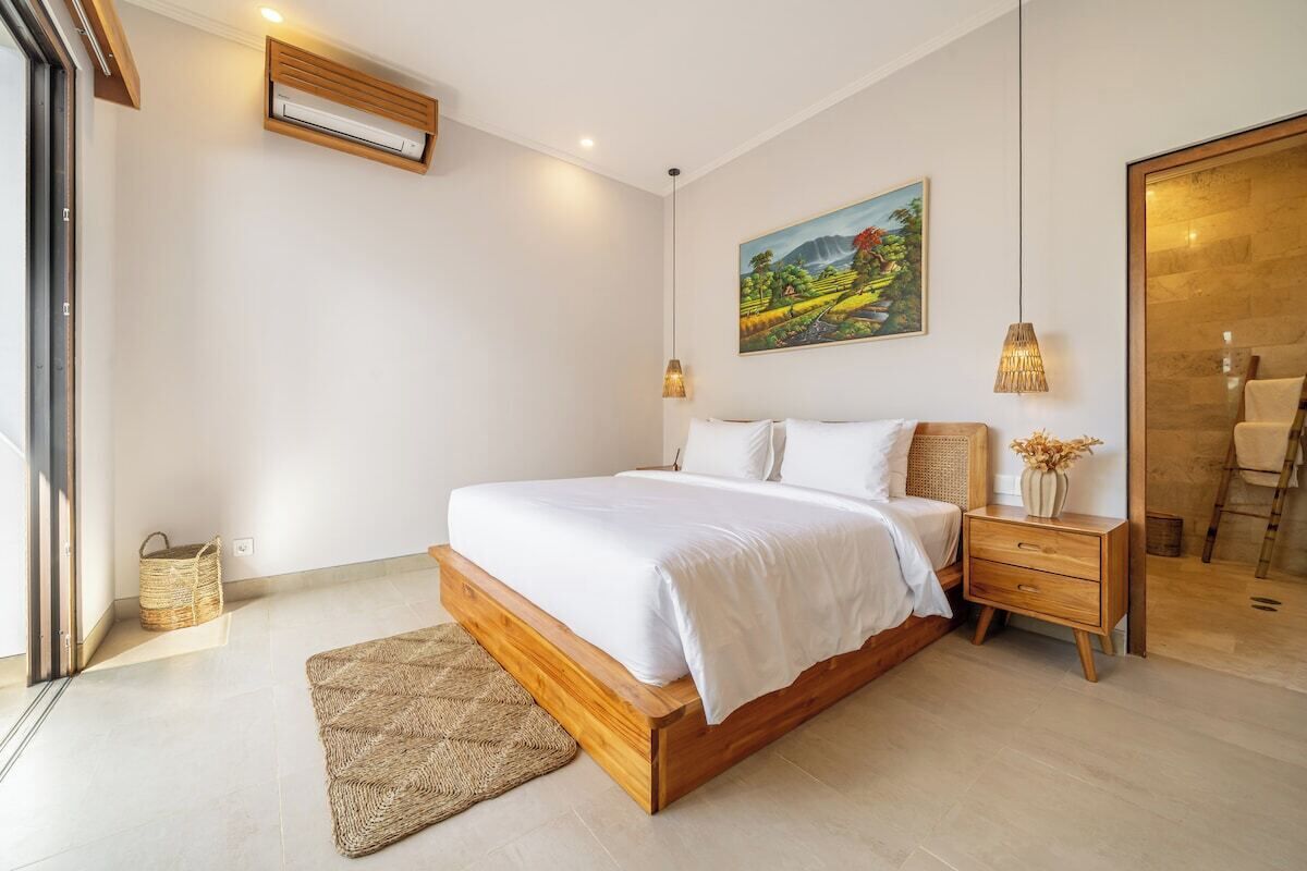 Un dormitorio con una cama grande, mesitas de noche, aire acondicionado de pared, un cuadro y vistas al exterior.