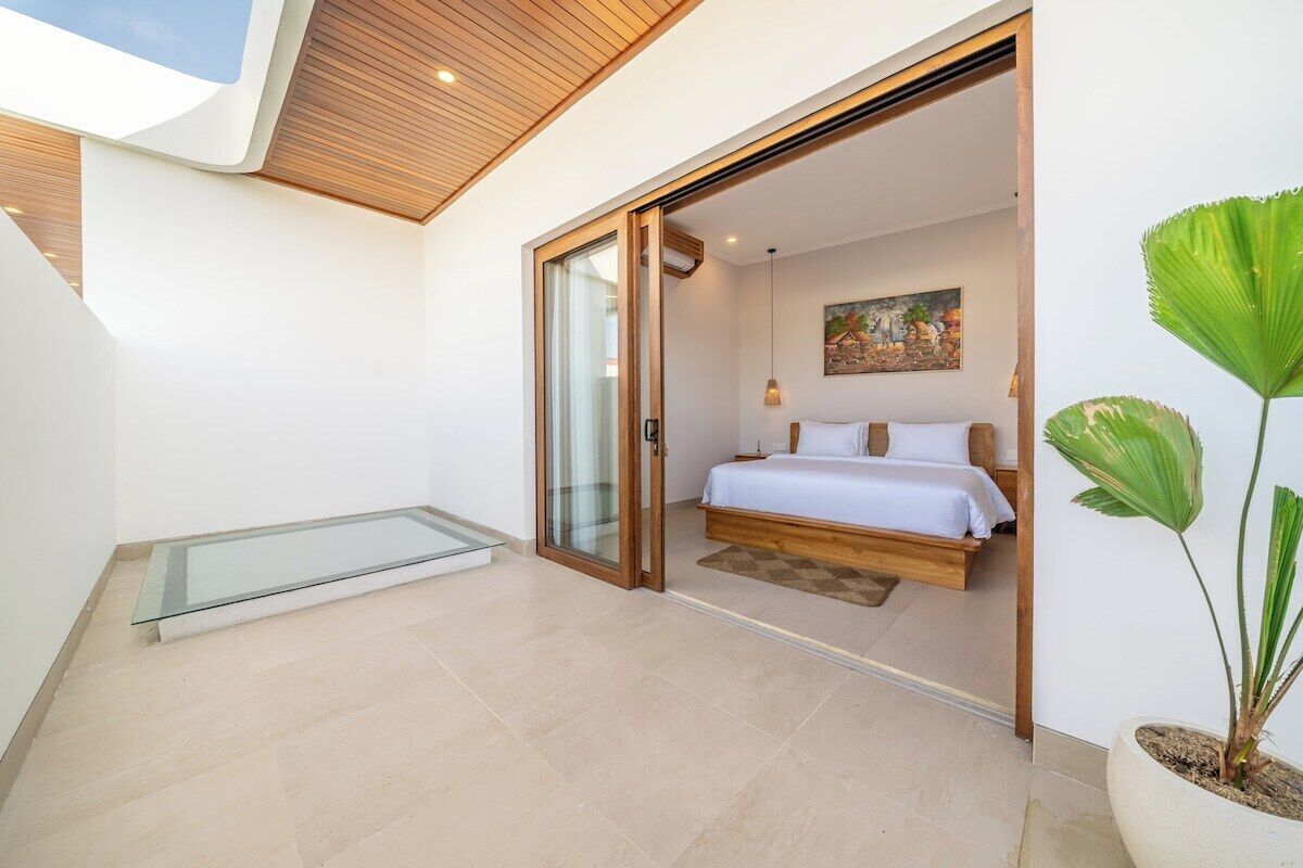 A bedroom with a bed, a glass door leading to a balcony, and a potted plant.