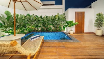 Ein Poolbereich mit Holzterrasse, Liegestuhl und großem Sonnenschirm.