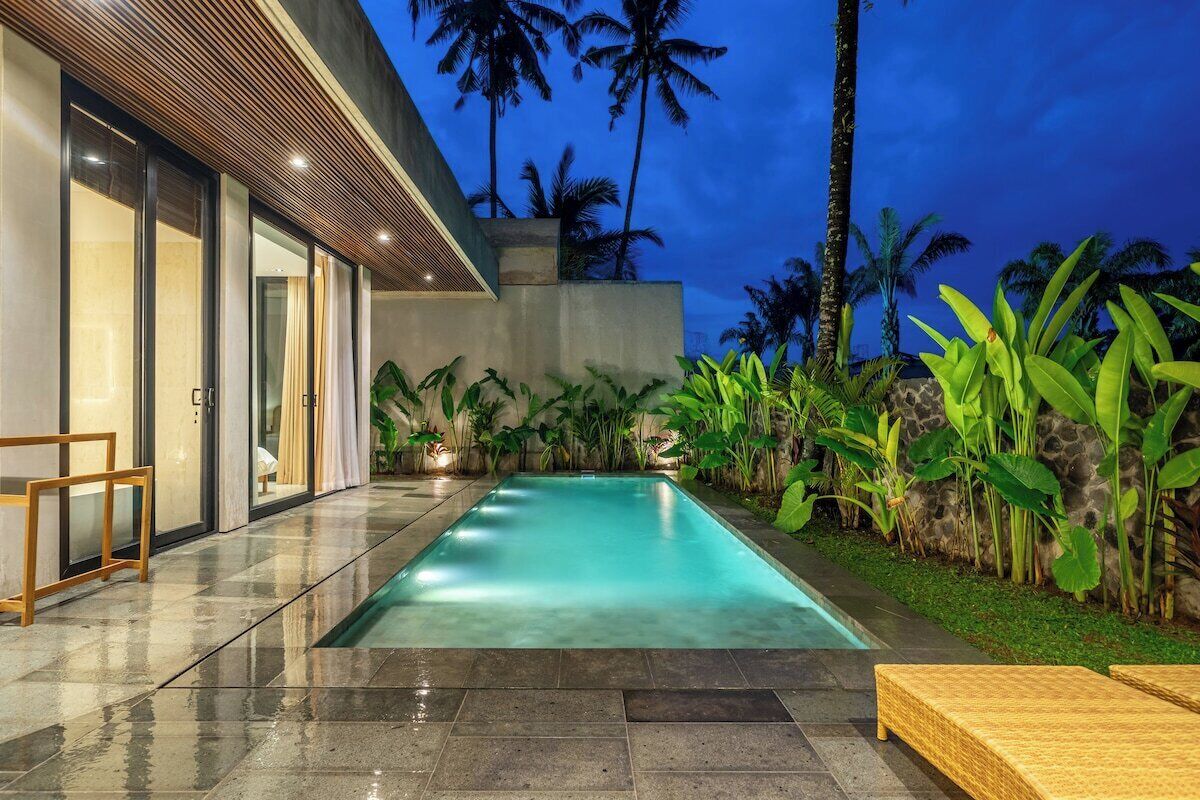 A swimming pool with a modern house in the background, surrounded by tropical plants.