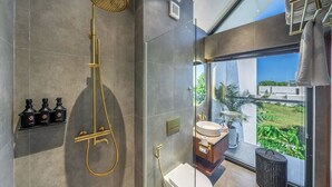 Et moderne badeværelse med en brusekabine i glas, toilet og vask med udsigt til grønne omgivelser.