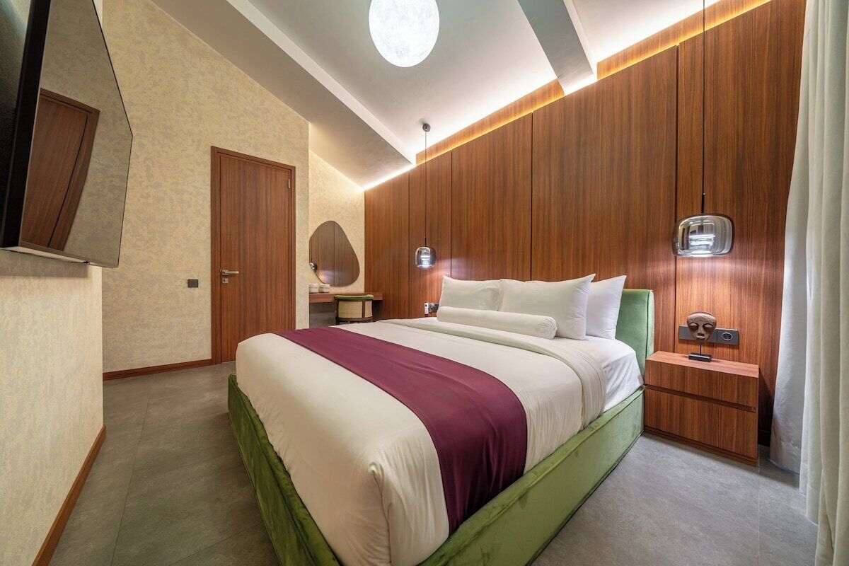 A hotel room with a bed, a nightstand, a mirror, and a wall-mounted TV.