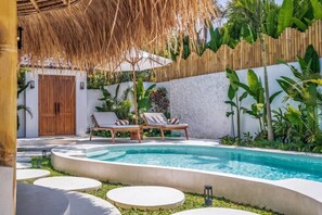 Ein Poolbereich mit Liegestühlen und einer Struktur mit Reetdach.