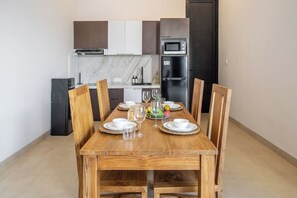 A dining area with a wooden table set for six, surrounded by chairs. A kitchen with modern appliances is visible in the background. - Cozy 2BR Villa • 300m to Sanur Beach+Pool+Rooftop (Kota Denpasar)