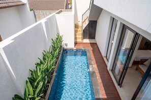 Una piscina con bordo in legno, circondata da pareti bianche e una scala che conduce a un livello superiore.