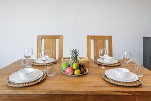 A wooden dining table set for four with white plates, bowls, and glasses, and a fruit centerpiece. - Cozy 2BR Villa • 300m to Sanur Beach+Pool+Rooftop (Kota Denpasar)