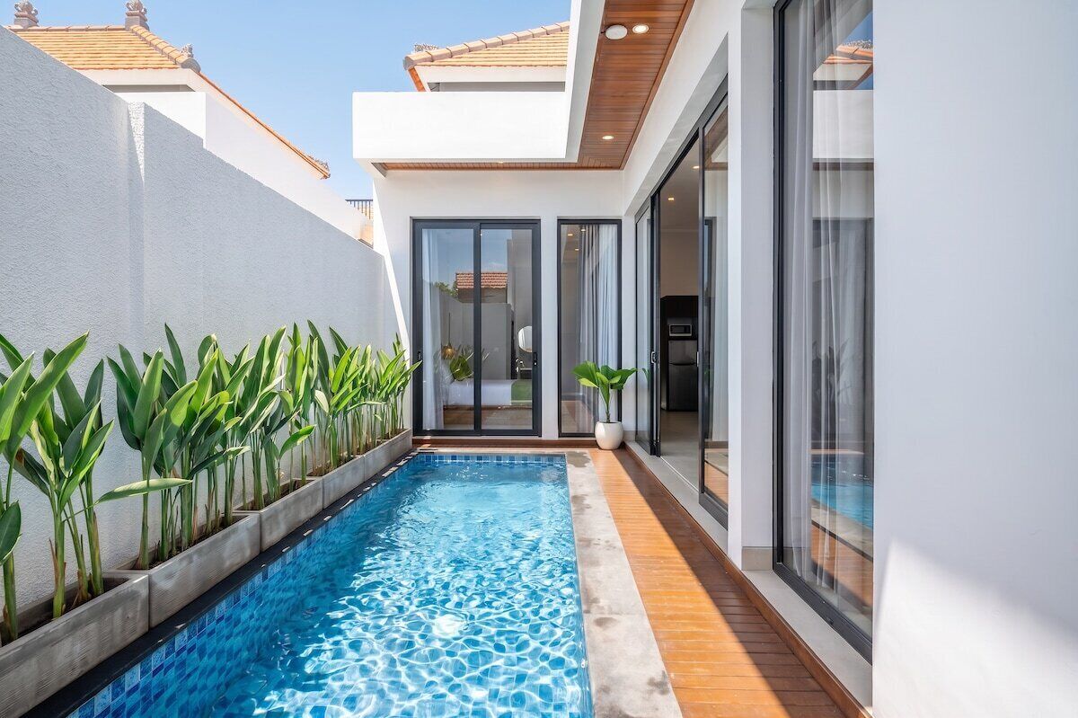 A modern residential building with a swimming pool, large windows, and a tiled deck.