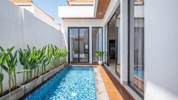 A modern residential building with a swimming pool, large windows, and a tiled deck.