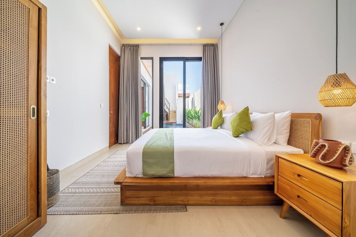 A modern bedroom with a large bed, wooden nightstand, and a view through a sliding door to an outdoor balcony.