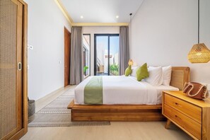 A modern bedroom with a large bed, wooden nightstand, and a view through a sliding door to an outdoor balcony. - Chic 2BR Villa in 300m to the Ocean w Pool+Rooftop (Kota Denpasar)