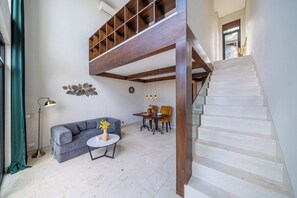 A modern interior with a staircase, a sofa, a dining table, and a decorative wall piece. - Cozy 1BR Gem in Ubud w Pool • Perfect for Couples! (Kabupaten Gianyar)