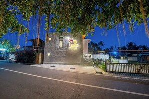 A gated entrance to Sunny Villas with a palm tree logo, a paved driveway, and a street with parked cars. - Cozy 1BR Gem in Ubud w Pool • Perfect for Couples! (Kabupaten Gianyar)