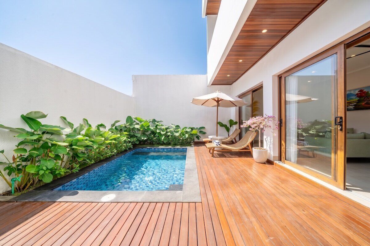 Ein moderner Poolbereich im Freien mit Holzterrasse, einem kleinen Pool und Liegestühlen.