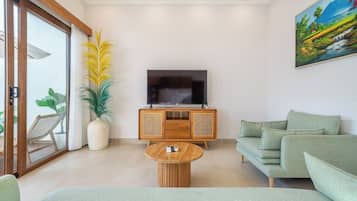 Ein modernes Wohnzimmer mit einem Flachbildfernseher, einem Holzschrank, einem grünen Sofa und einer großen Küstertopf-Pflanze.