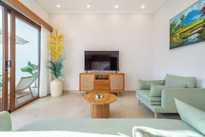 Een moderne woonkamer met een flatscreen televisie, een houten kast, een groene bank en een grote kamerplant.