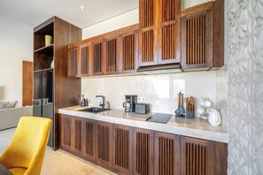 A modern kitchen with wooden cabinetry, a built-in island with a sink, and a yellow chair. - Spacious 2BR Villa w Pool, Garden & Balcony • Ubud (Kabupaten Gianyar)