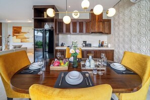 A dining area with a wooden table set for four, surrounded by yellow chairs, and a kitchen in the background. - Spacious 2BR Villa w Pool, Garden & Balcony • Ubud (Kabupaten Gianyar)