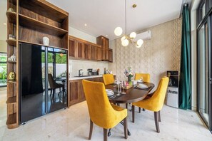 A modern dining area with a dark wooden table, yellow chairs, and a glass partition separating the dining space from the kitchen. - Tropical 2BR in Ubud w Pool, Huge Garden & Balcony (Ubud)