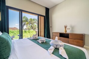 A hotel room with a bed, a wooden nightstand, and a view of greenery outside. - Tropical 2BR in Ubud w Pool, Huge Garden & Balcony (Ubud)