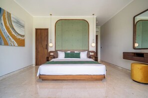Ein Hotelzimmer mit einem großen Bett, einem hölzernen Kopfteil, einem grünen Zierkissen, einem gelben Pouf und einem großen Spiegel.