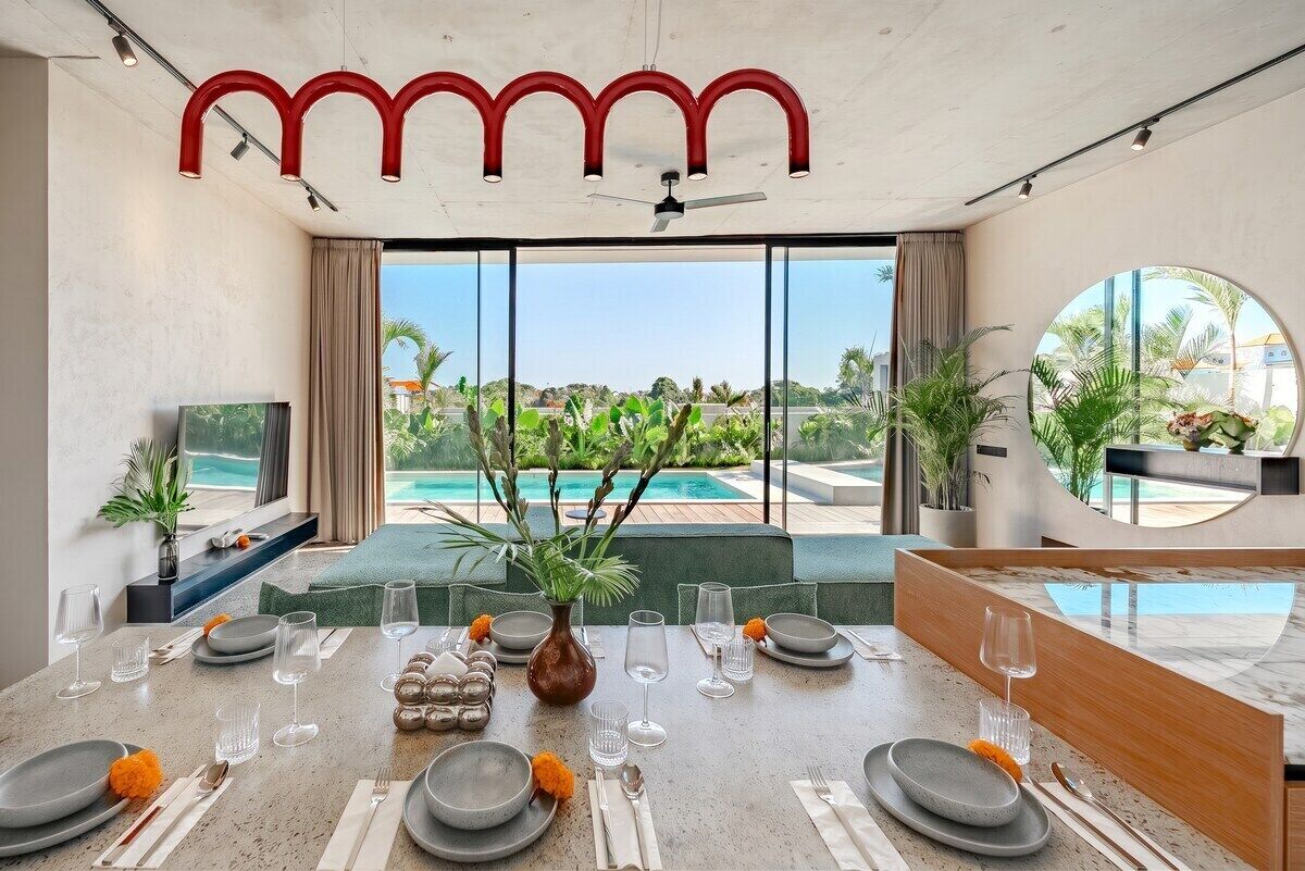 A dining area with a view of a swimming pool and greenery.